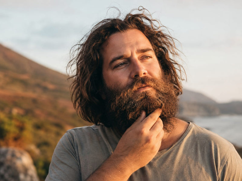 Man with a full thick beard outdoors at golden hour near coastal hills