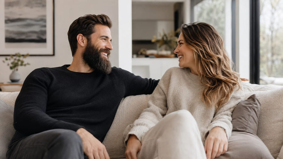 Man with a full groomed dark beard sitting with a partner on a living room sofa