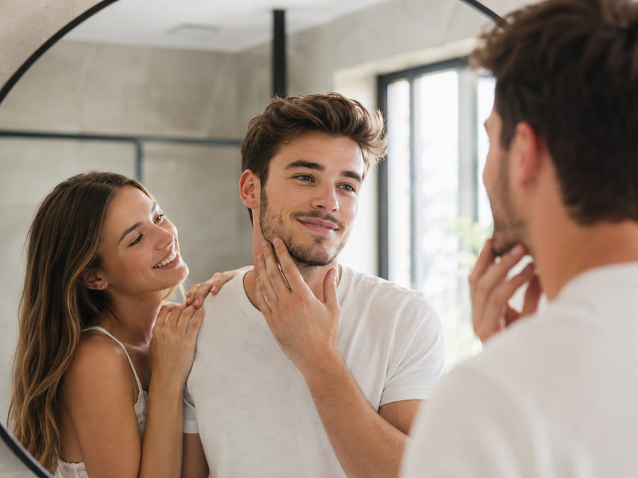Man with a short beard checking his jawline in a bathroom mirror