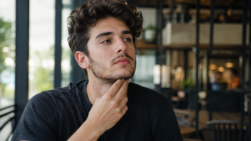 Man with patchy cheek gaps checking his beard in a bathroom mirror